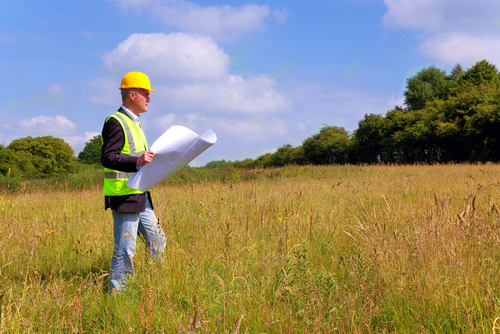 Architect,Wearing,Site,Safety,Gear,And,Holding,Plans,Surveying,A man surveying